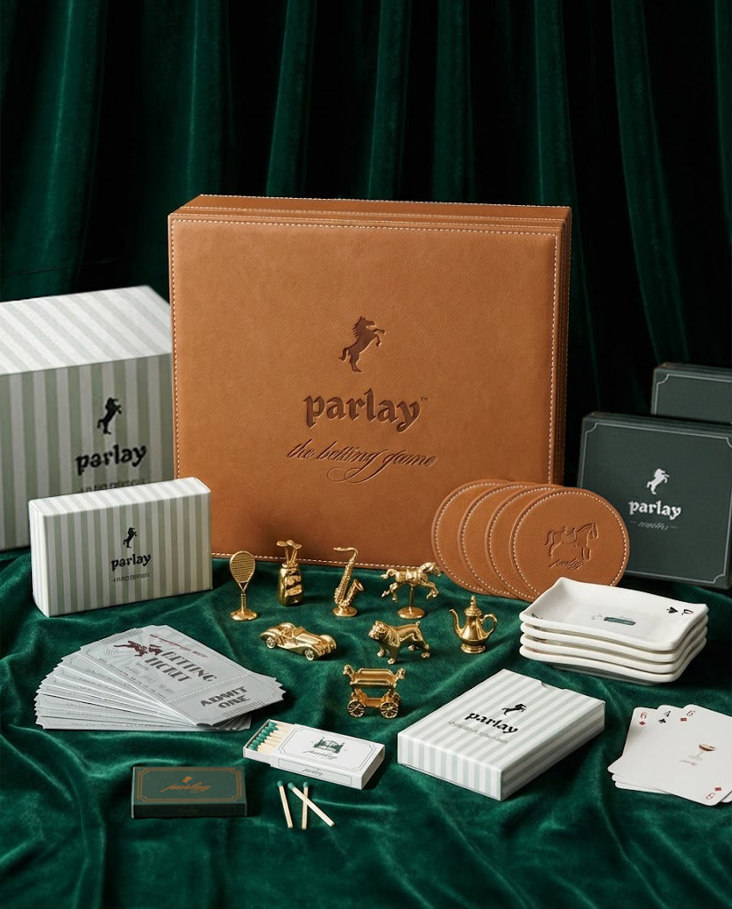 The Parlay Deluxe Hosting Set arranged on emerald velvet — leather-bound board, gold pawns, betting tickets, and coasters